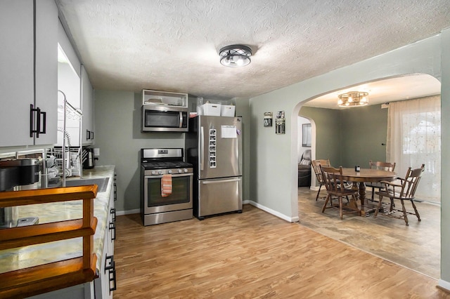 kitchen featuring arched walkways, a textured ceiling, stainless steel appliances, baseboards, and light wood-style floors