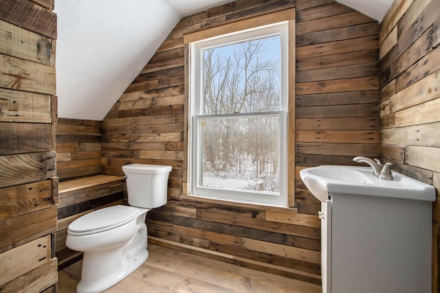 half bathroom featuring lofted ceiling, wood walls, vanity, and toilet