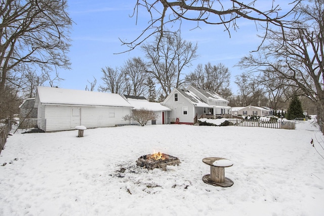 snow covered back of property with a fire pit, a detached garage, and fence