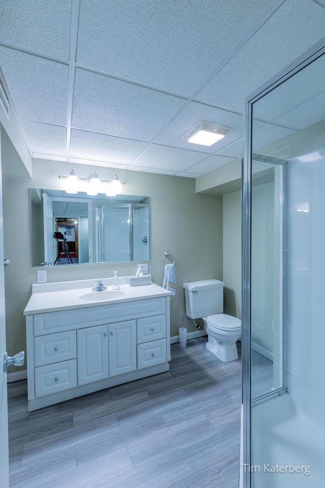 full bath featuring toilet, a shower stall, vanity, wood finished floors, and a drop ceiling