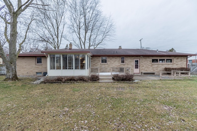 back of house featuring brick siding, a chimney, a lawn, a sunroom, and a deck