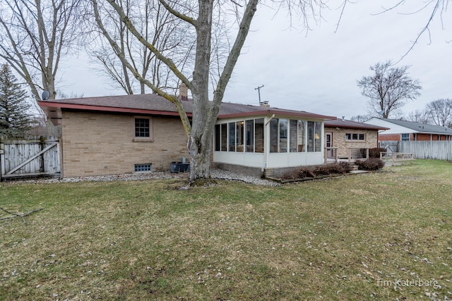 rear view of house with brick siding, fence, a sunroom, a lawn, and a chimney