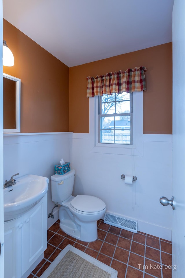 half bathroom featuring toilet, a wainscoted wall, visible vents, and tile patterned floors