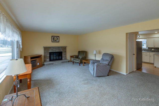 living area with light carpet, baseboards, and a stone fireplace