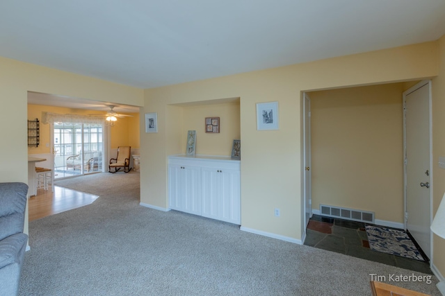 unfurnished living room with carpet floors, a ceiling fan, visible vents, and baseboards