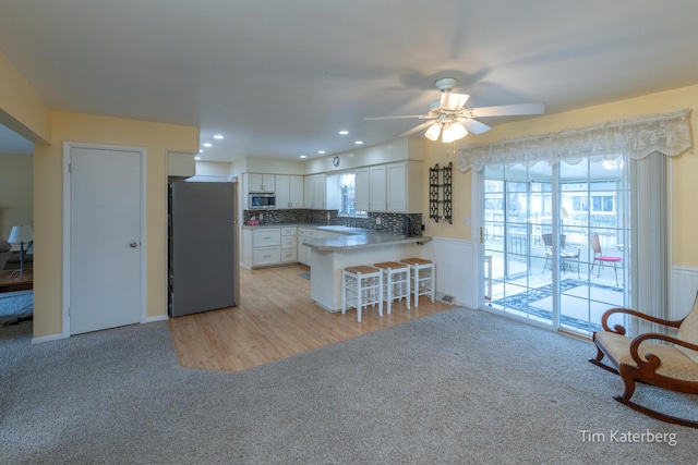 kitchen with tasteful backsplash, appliances with stainless steel finishes, light carpet, white cabinetry, and a peninsula