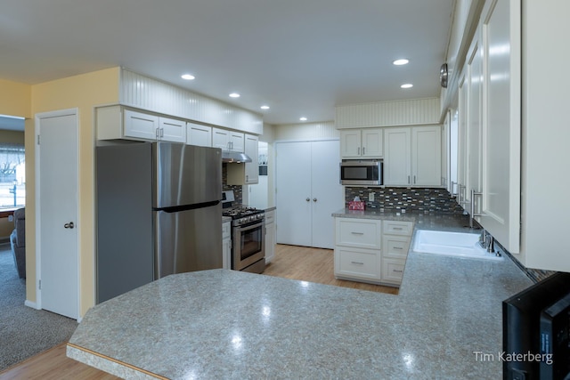 kitchen with under cabinet range hood, a peninsula, a sink, appliances with stainless steel finishes, and backsplash