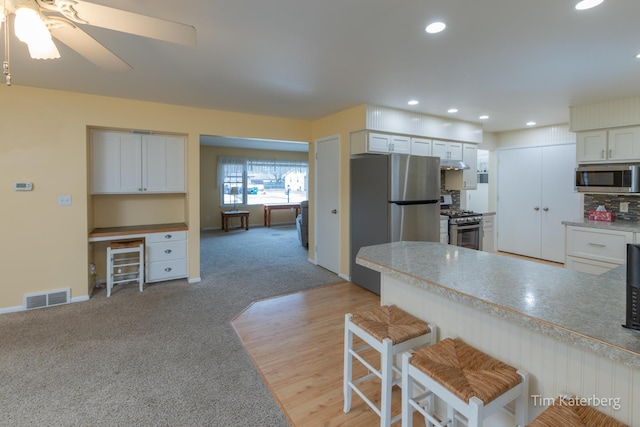 kitchen with appliances with stainless steel finishes, built in study area, visible vents, and light colored carpet