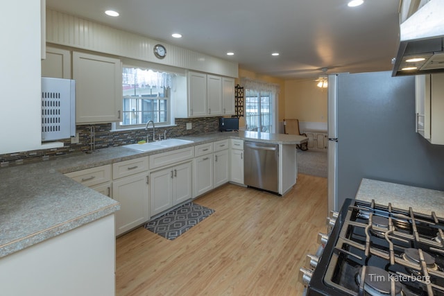 kitchen featuring light wood finished floors, appliances with stainless steel finishes, a sink, ventilation hood, and a peninsula