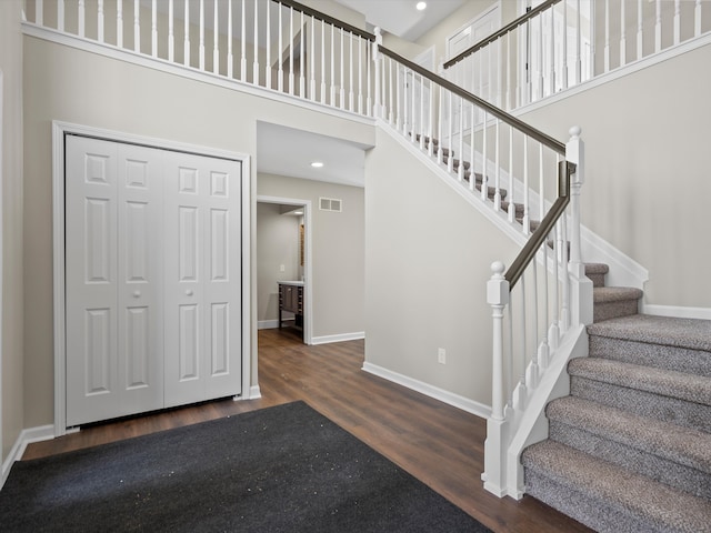 foyer entrance featuring a high ceiling, wood finished floors, visible vents, baseboards, and stairway