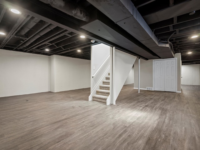 finished basement featuring visible vents, stairway, and wood finished floors