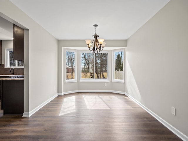 unfurnished dining area featuring a sink, baseboards, a chandelier, and dark wood-type flooring