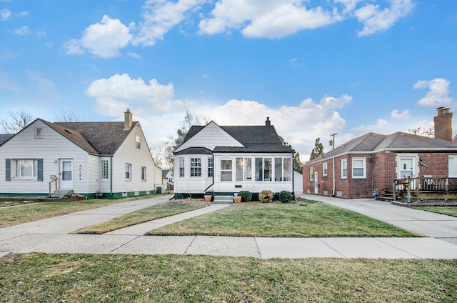 bungalow-style house with entry steps, a sunroom, a front lawn, and concrete driveway