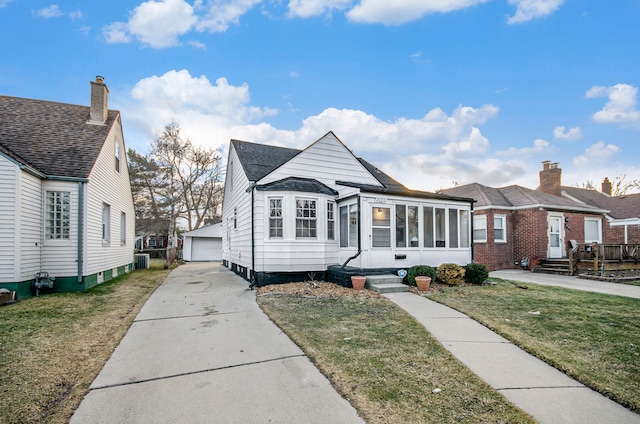 view of front of home with an outbuilding, a detached garage, central air condition unit, a front yard, and a sunroom