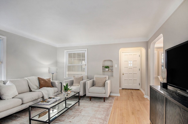 living room featuring arched walkways, light wood-style flooring, and baseboards