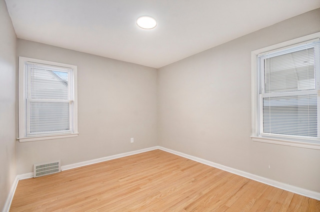 spare room featuring light wood-style floors, visible vents, and baseboards