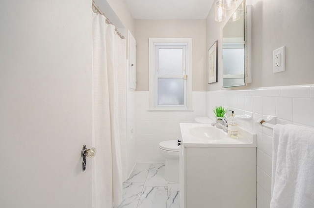 bathroom with marble finish floor, tile walls, toilet, wainscoting, and vanity