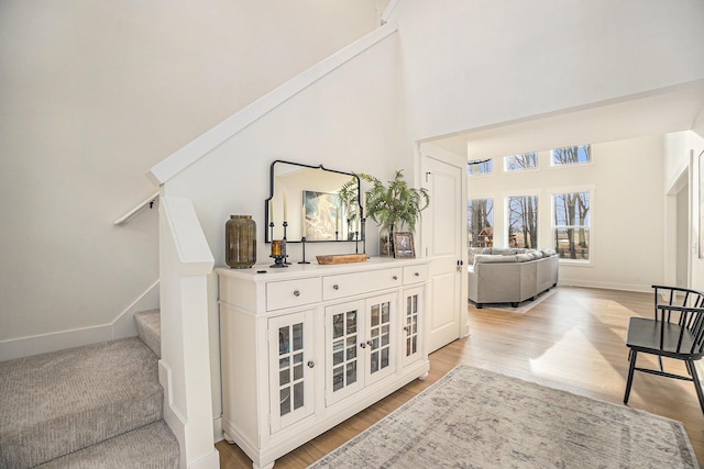 foyer entrance with stairway, light wood-type flooring, a towering ceiling, and baseboards