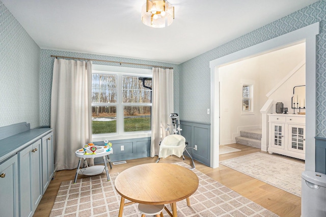 living area featuring visible vents, wallpapered walls, light wood-style floors, wainscoting, and stairs