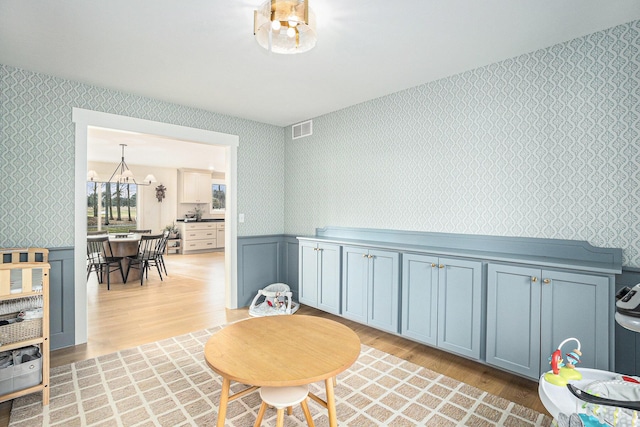 living area with light wood-type flooring, wainscoting, visible vents, and wallpapered walls