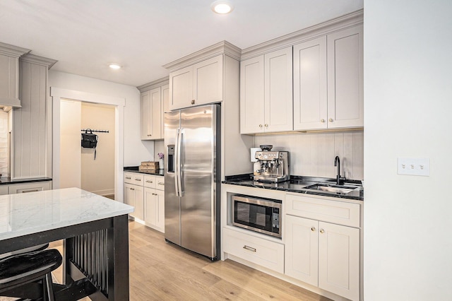 kitchen featuring recessed lighting, a sink, appliances with stainless steel finishes, light wood-type flooring, and dark stone countertops