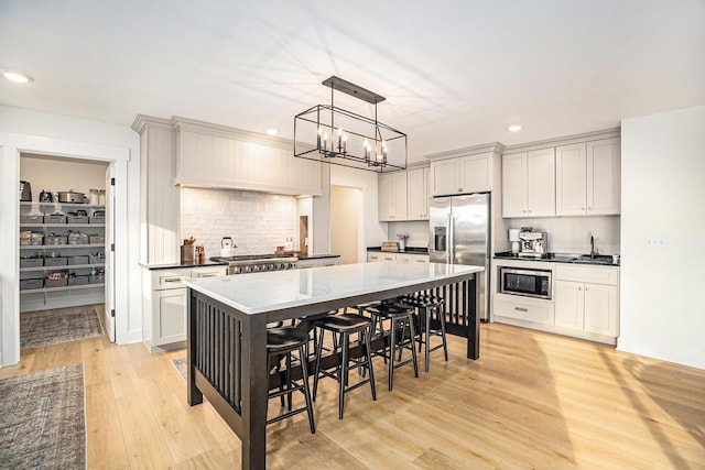 kitchen featuring a breakfast bar area, a kitchen island, appliances with stainless steel finishes, decorative backsplash, and light wood finished floors