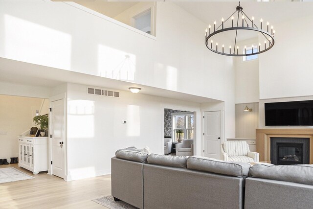 living area featuring visible vents, a glass covered fireplace, a high ceiling, light wood-style floors, and a chandelier