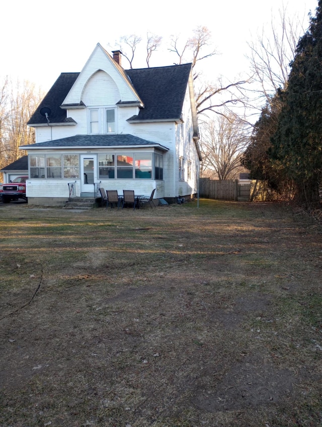 view of front facade with entry steps, a shingled roof, a chimney, fence, and a front yard