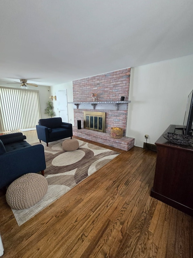 living room with ceiling fan, a brick fireplace, and wood finished floors