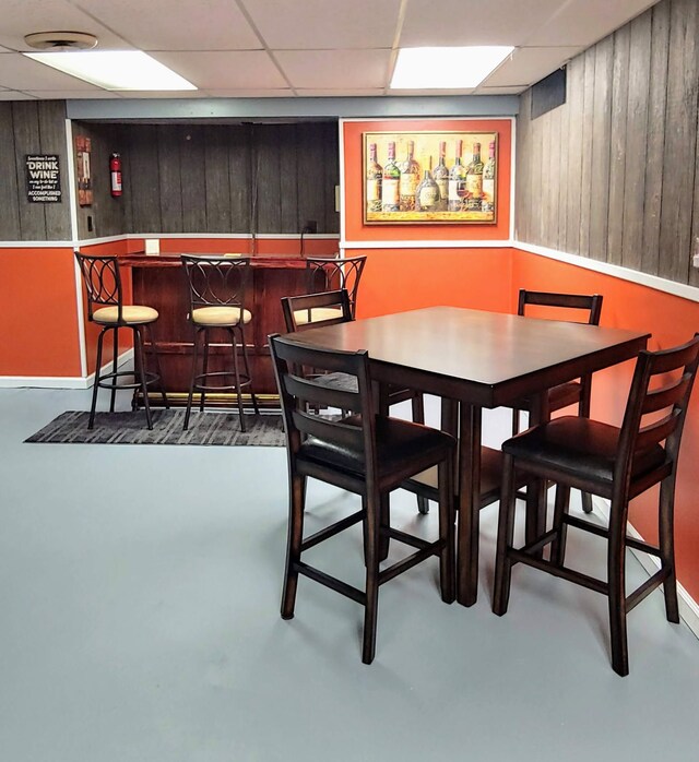 dining space with a bar, wooden walls, finished concrete floors, and a paneled ceiling