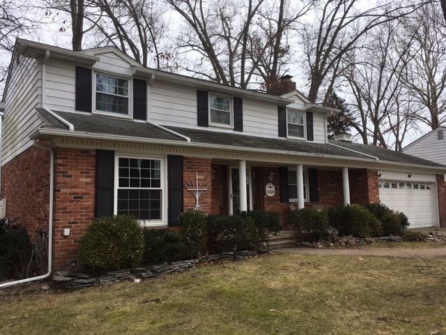 view of front of property with a garage, a chimney, covered porch, a front lawn, and brick siding