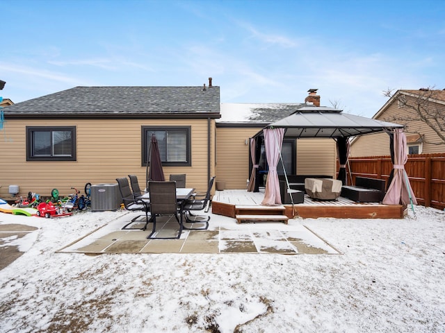 snow covered back of property featuring central air condition unit, a shingled roof, a gazebo, fence, and a wooden deck