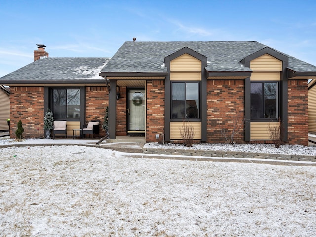 view of front of property featuring a shingled roof, brick siding, and a chimney