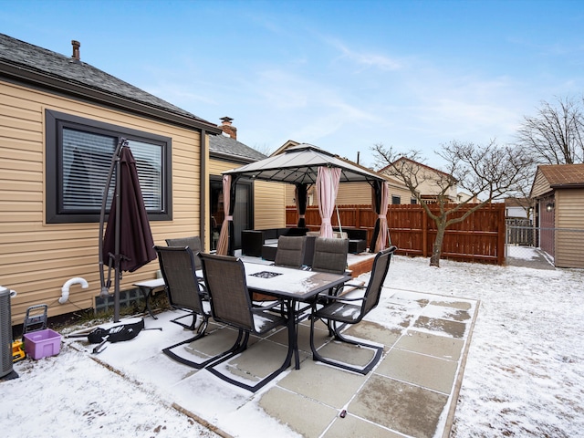 snow covered patio featuring a gazebo, outdoor dining area, and fence