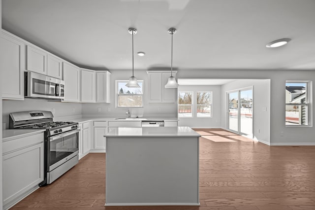 kitchen featuring white cabinets, a kitchen island, wood finished floors, stainless steel appliances, and a sink