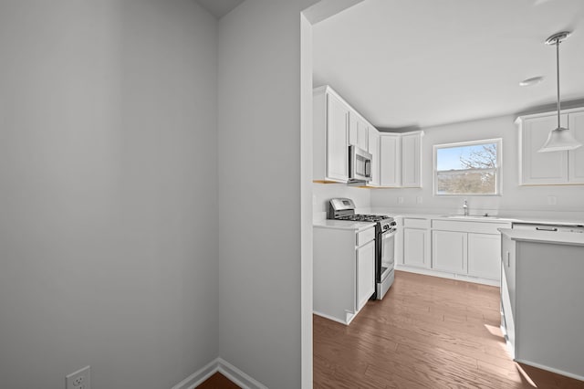 kitchen with light countertops, appliances with stainless steel finishes, white cabinetry, a sink, and light wood-type flooring