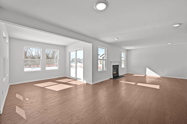 unfurnished living room featuring a wealth of natural light, a glass covered fireplace, baseboards, and wood finished floors