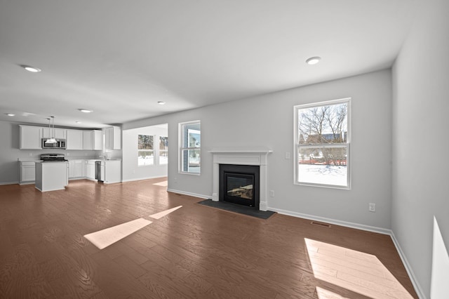 unfurnished living room featuring a fireplace with flush hearth, visible vents, baseboards, and dark wood finished floors