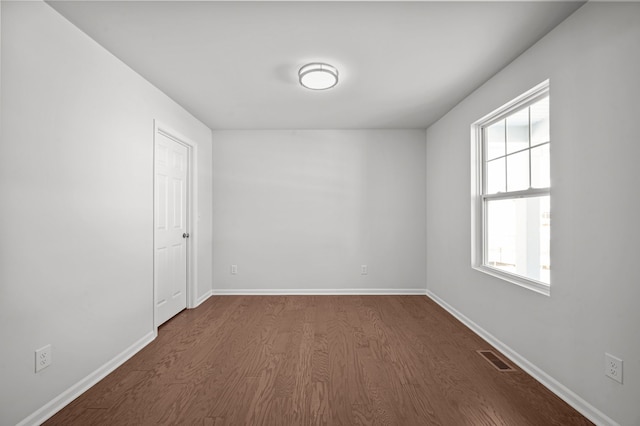 unfurnished room with baseboards, visible vents, and dark wood finished floors