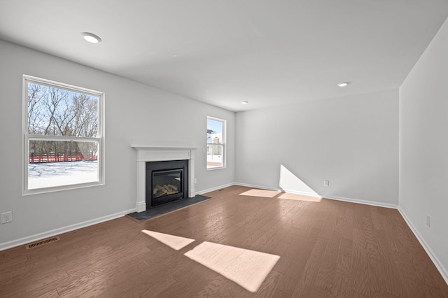 unfurnished living room featuring dark wood-style floors, baseboards, visible vents, and a glass covered fireplace