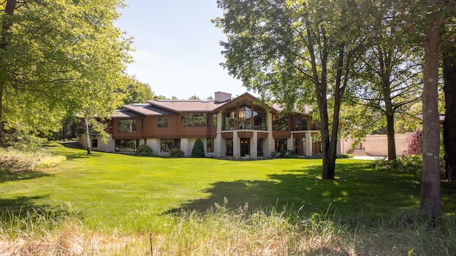 rear view of property with stone siding, a lawn, and a chimney