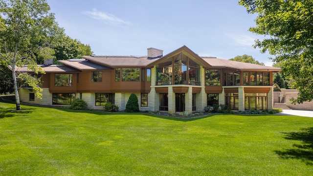 back of house with a sunroom, a chimney, stone siding, and a yard