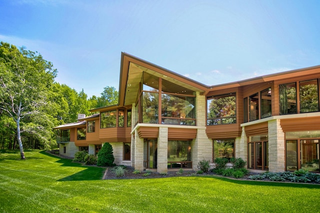 back of property featuring stone siding and a lawn