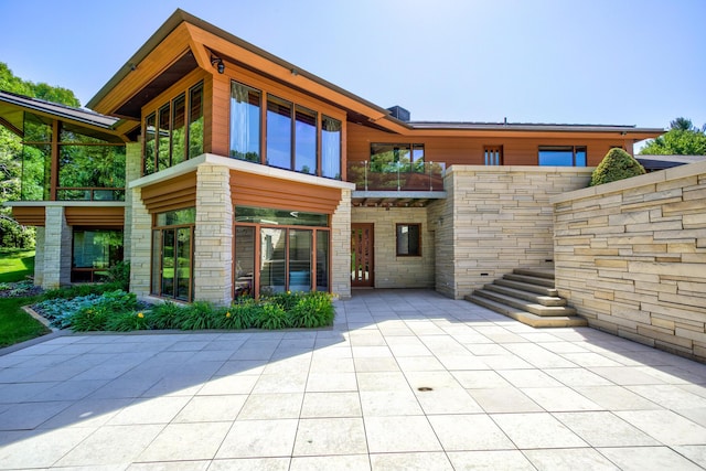 back of property with stone siding, a patio, and a balcony