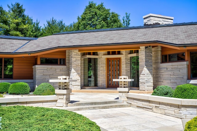 property entrance with a shingled roof and stone siding