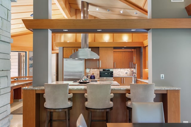 kitchen with appliances with stainless steel finishes, brown cabinets, light stone counters, and tasteful backsplash