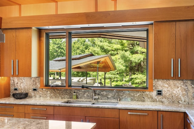 kitchen with light stone countertops, tasteful backsplash, brown cabinets, and a sink