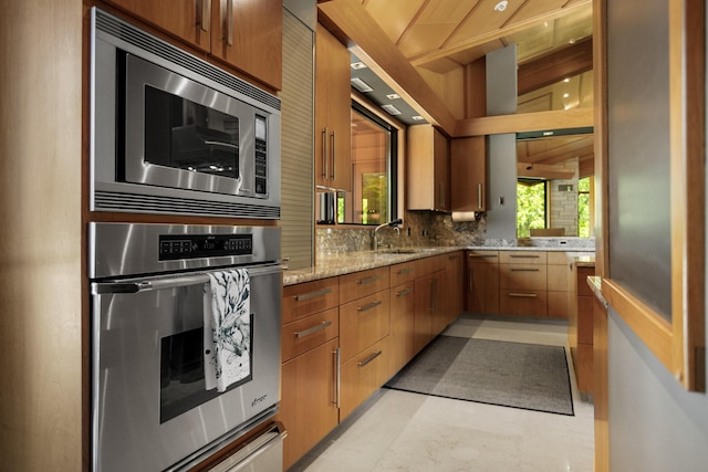 kitchen featuring stainless steel appliances, tasteful backsplash, brown cabinetry, and a sink