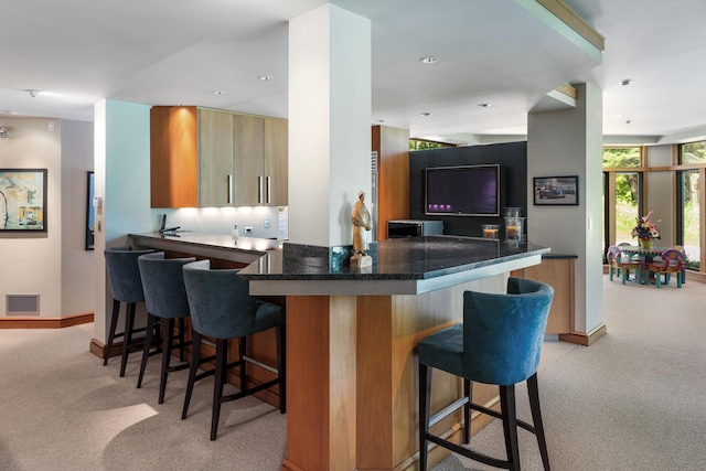 kitchen featuring visible vents, light carpet, a kitchen breakfast bar, and a peninsula