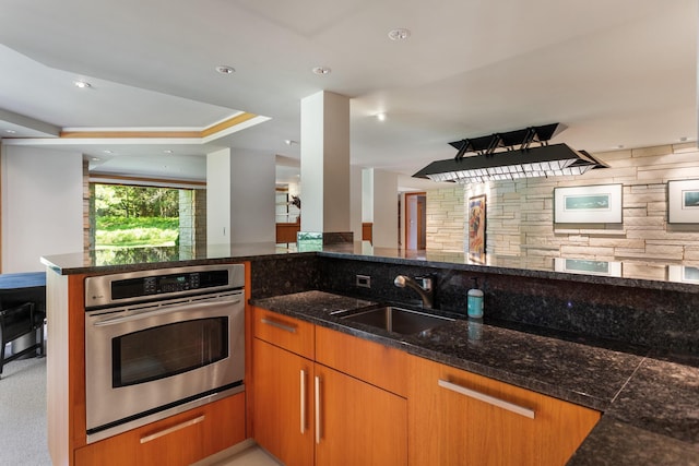 kitchen featuring brown cabinets, recessed lighting, stainless steel oven, a sink, and dark stone counters